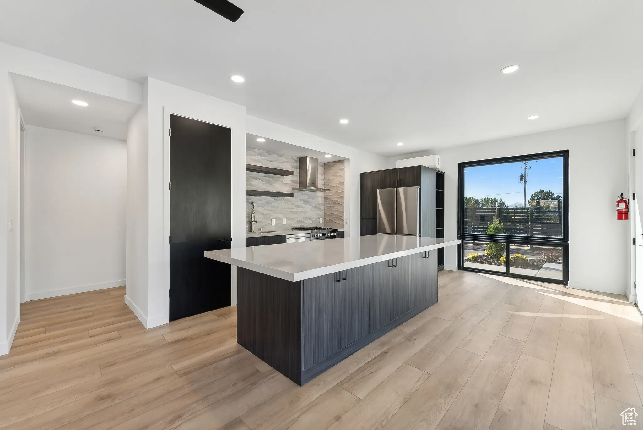 Kitchen featuring light wood-type flooring, tasteful backsplash, stainless steel stove, a kitchen island, and wall chimney exhaust hood