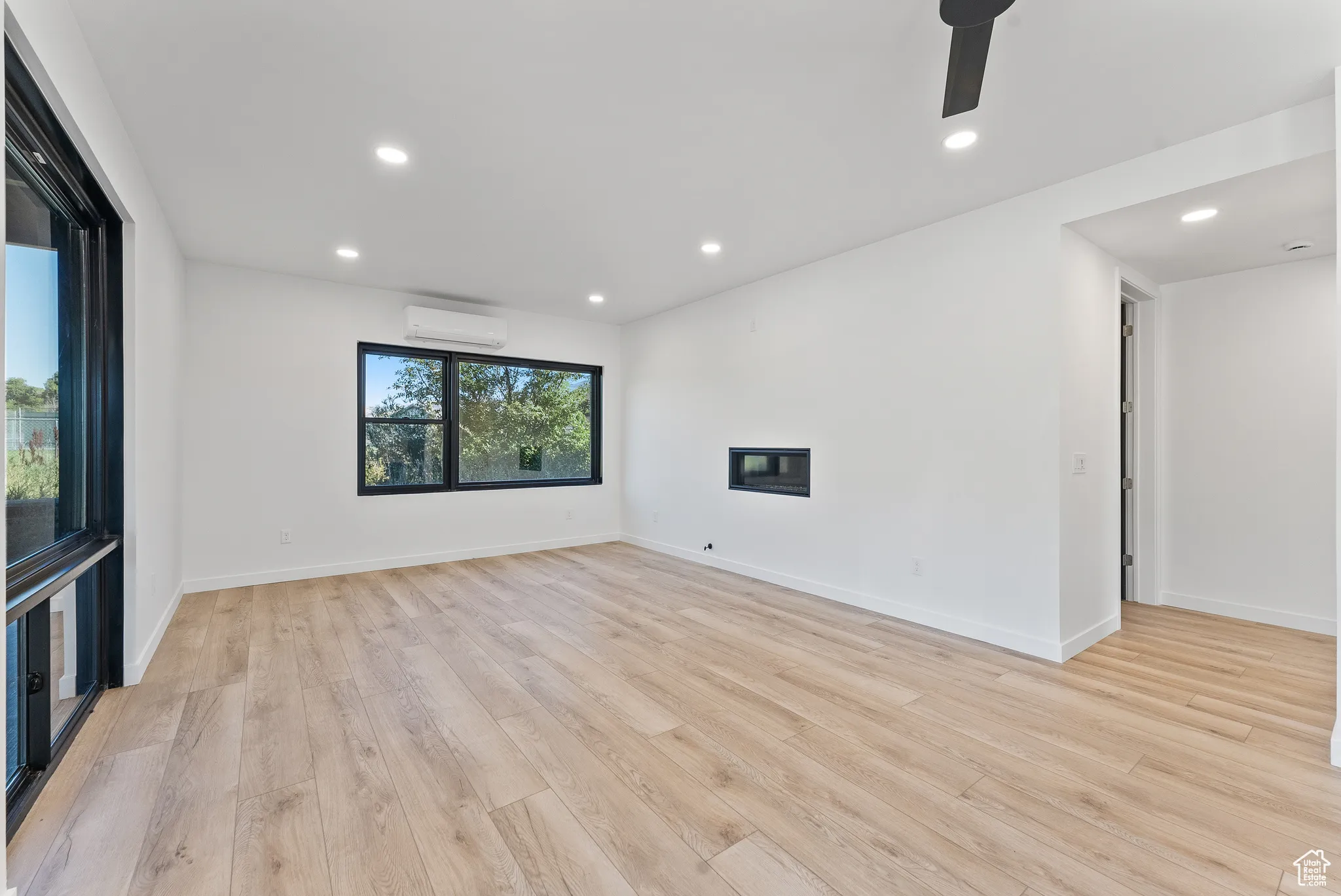 Spare room featuring light hardwood / wood-style floors, ceiling fan, a wall mounted AC, and a wealth of natural light