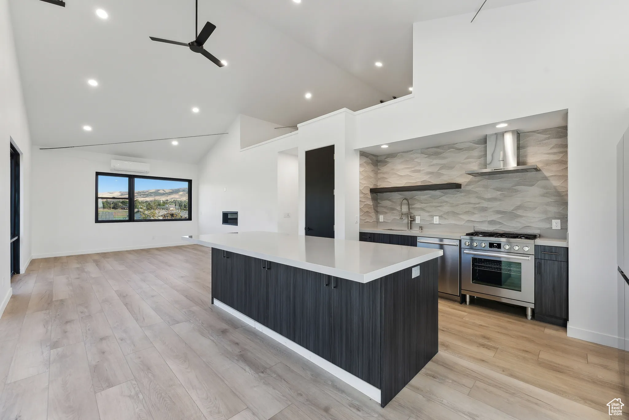 Kitchen with ceiling fan, sink, a large island, stainless steel appliances, and light hardwood / wood-style floors