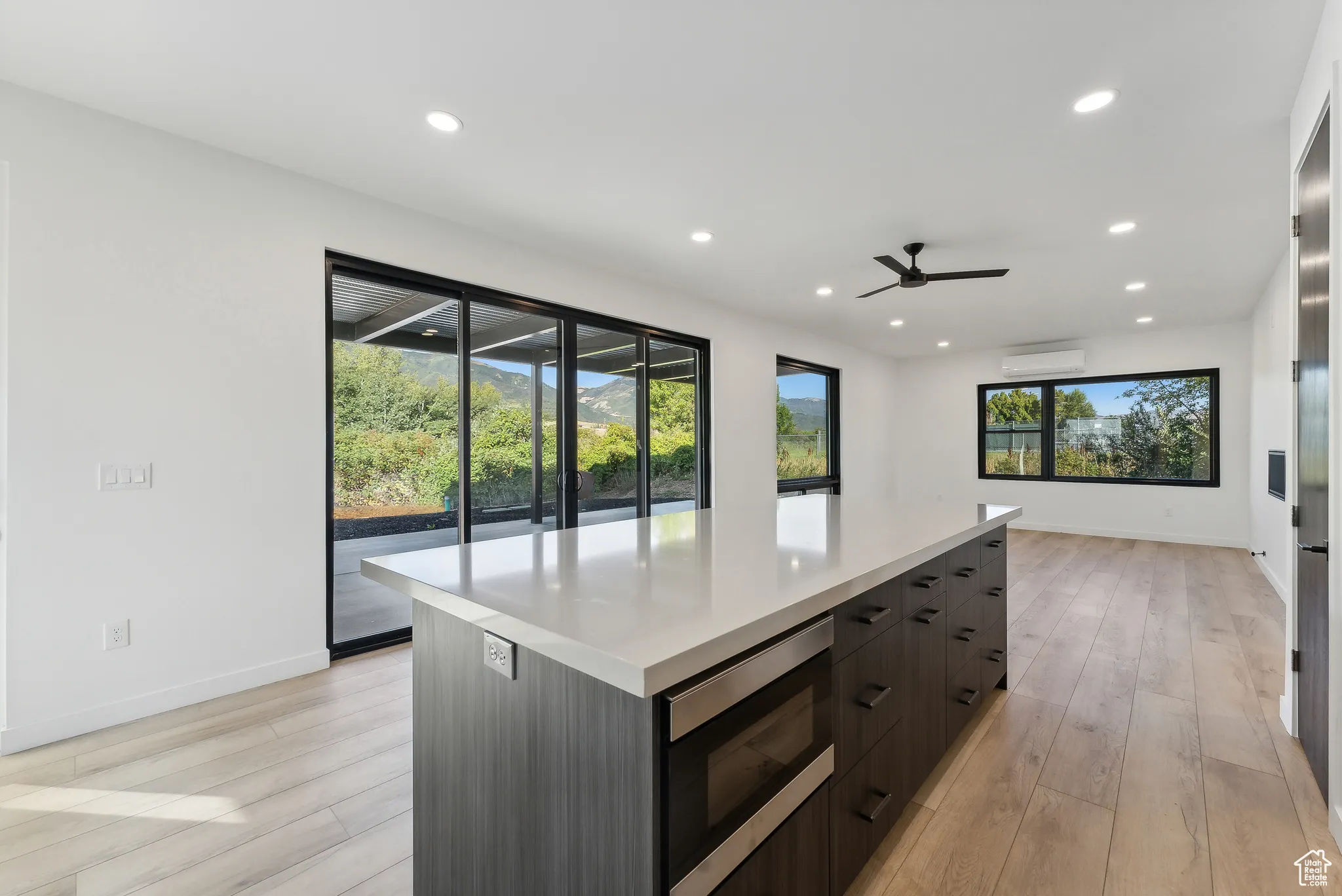 Kitchen with stainless steel microwave, an AC wall unit, light wood-type flooring, ceiling fan, and a large island