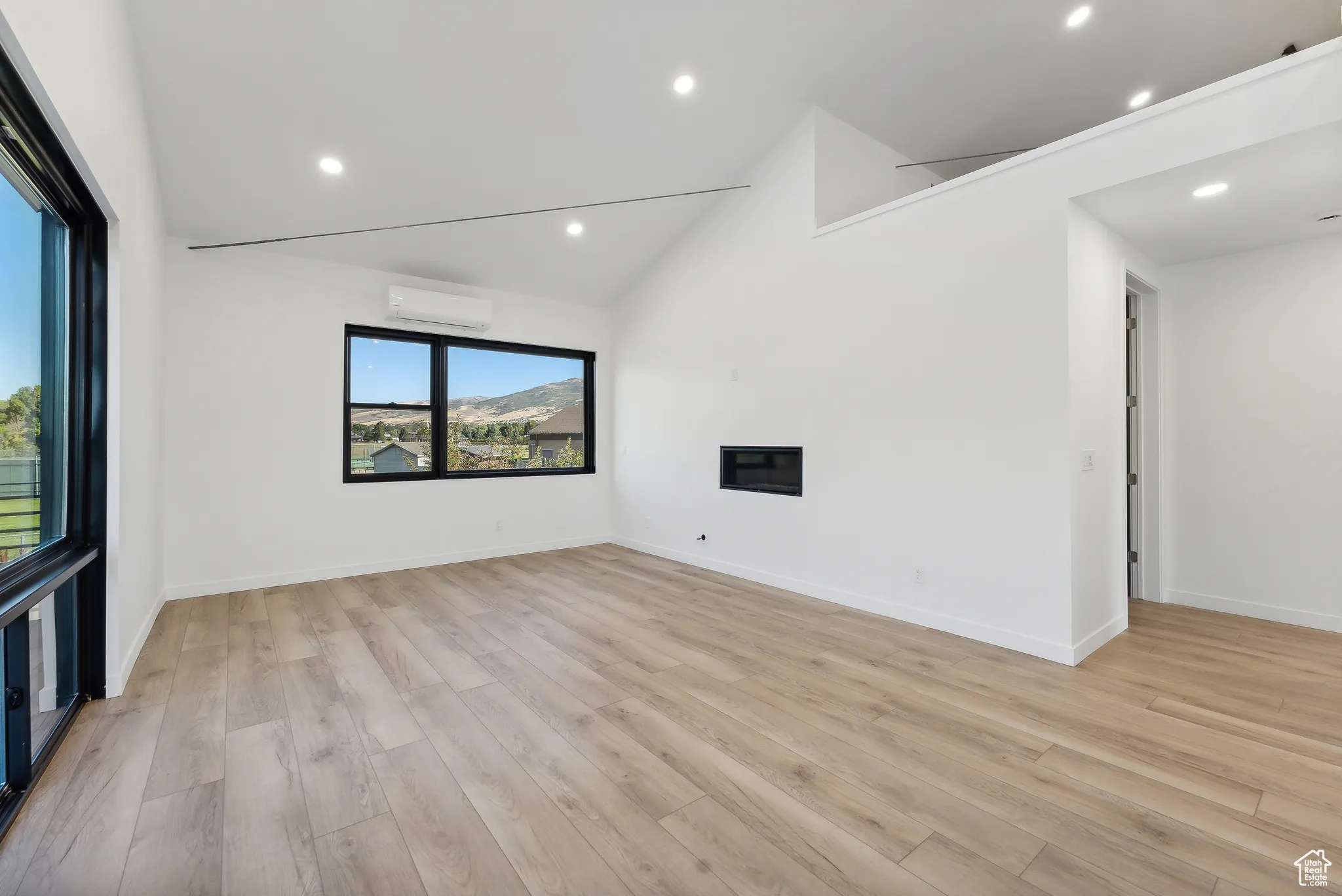 Unfurnished living room with a healthy amount of sunlight, vaulted ceiling, an AC wall unit, and light hardwood / wood-style flooring