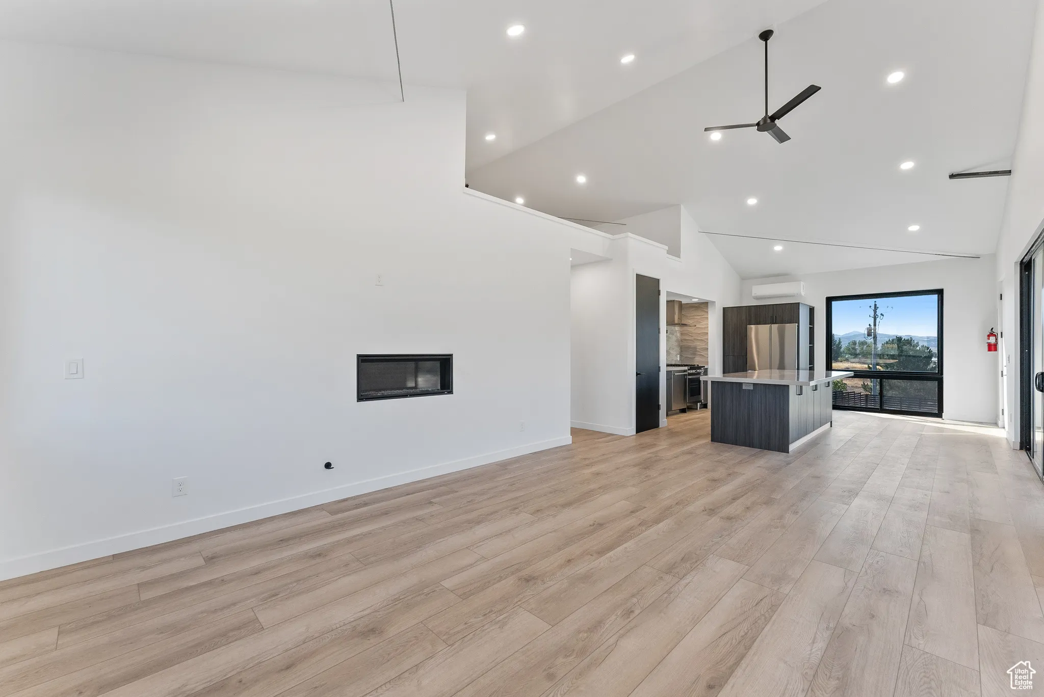 Unfurnished living room with light hardwood / wood-style floors, a wall mounted AC, ceiling fan, and high vaulted ceiling