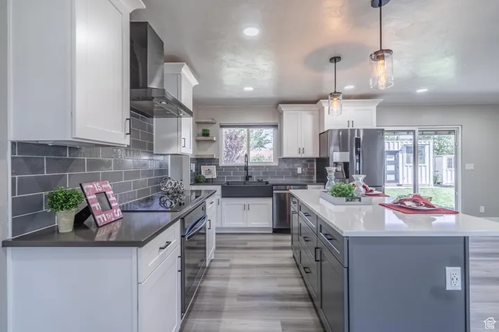 Kitchen featuring pendant lighting, light hardwood / wood-style flooring, wall chimney range hood, white cabinetry, and appliances with stainless steel finishes