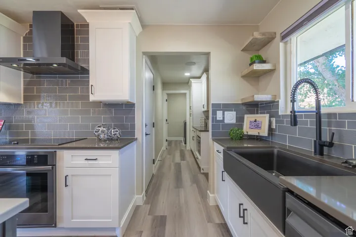 Kitchen featuring white cabinetry, wall chimney range hood, light hardwood / wood-style flooring, stainless steel appliances, and backsplash