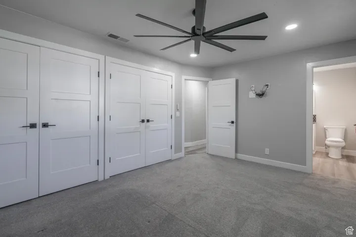 Unfurnished bedroom featuring carpet flooring, ceiling fan, ensuite bathroom, and multiple closets