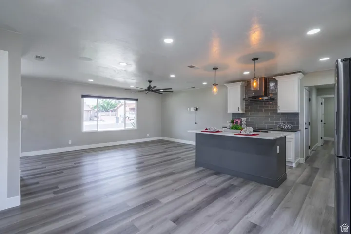 Kitchen with wood-type flooring, white cabinetry, a kitchen island, wall chimney exhaust hood, and decorative light fixtures