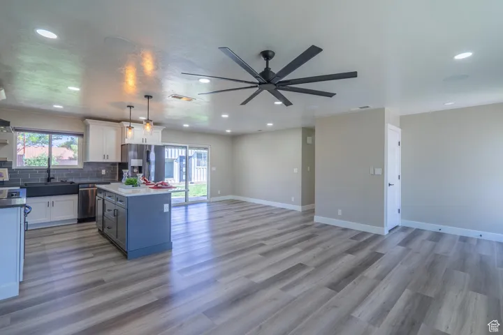 Kitchen with light hardwood / wood-style floors, a kitchen island, stainless steel appliances, ceiling fan, and decorative light fixtures