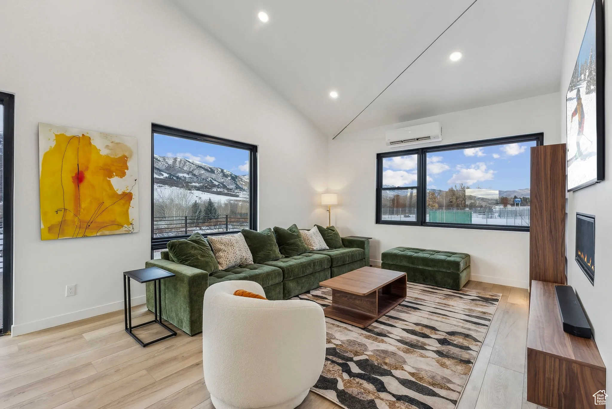 Living room with light hardwood / wood-style flooring, high vaulted ceiling, and a wall mounted air conditioner