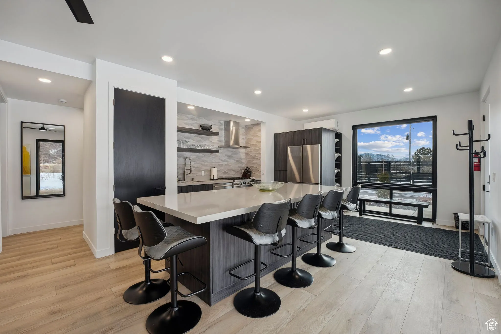 Kitchen featuring wall chimney exhaust hood, light hardwood / wood-style floors, sink, and a breakfast bar area