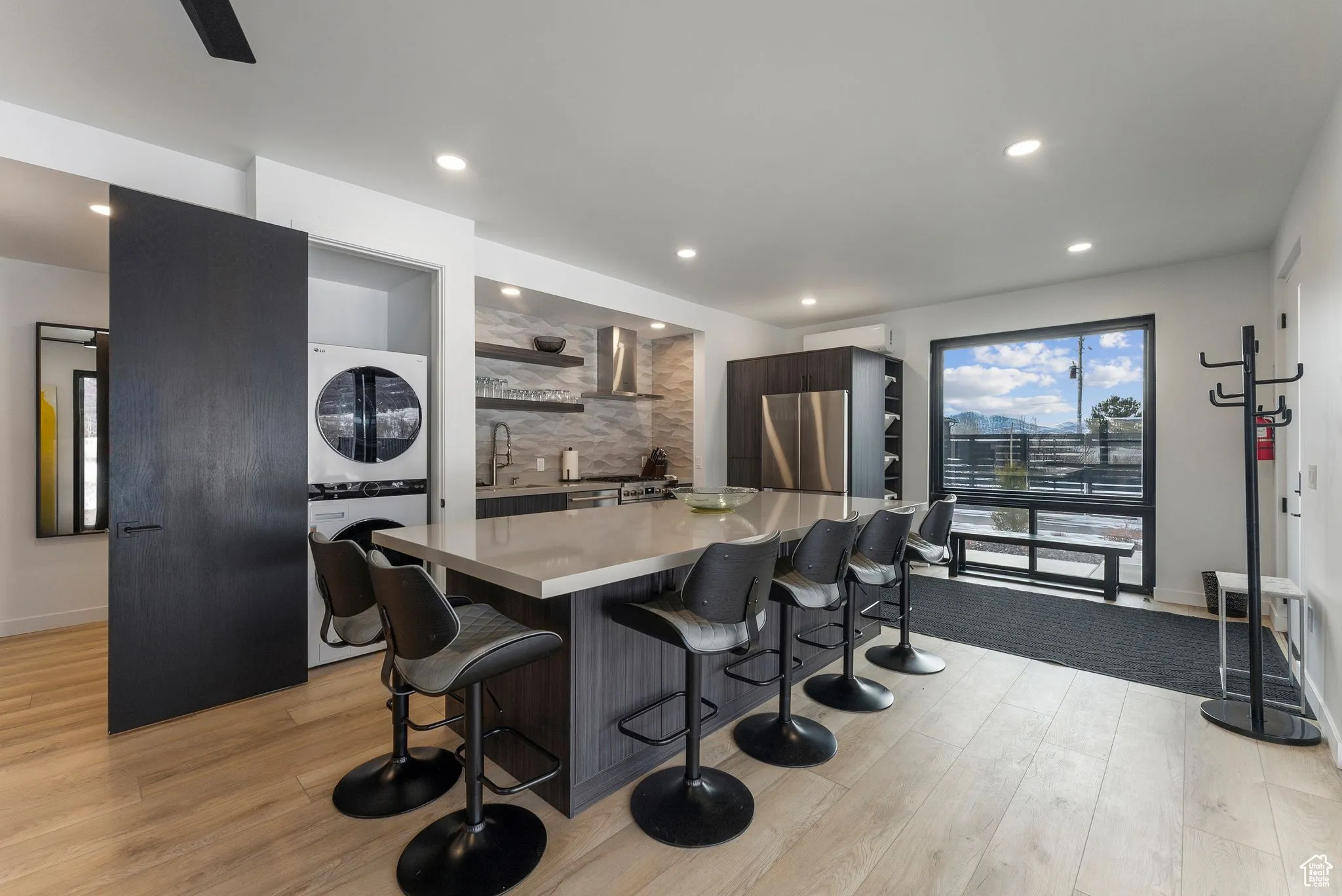 Kitchen with a kitchen breakfast bar, light wood-type flooring, stacked washing maching and dryer, and wall chimney range hood