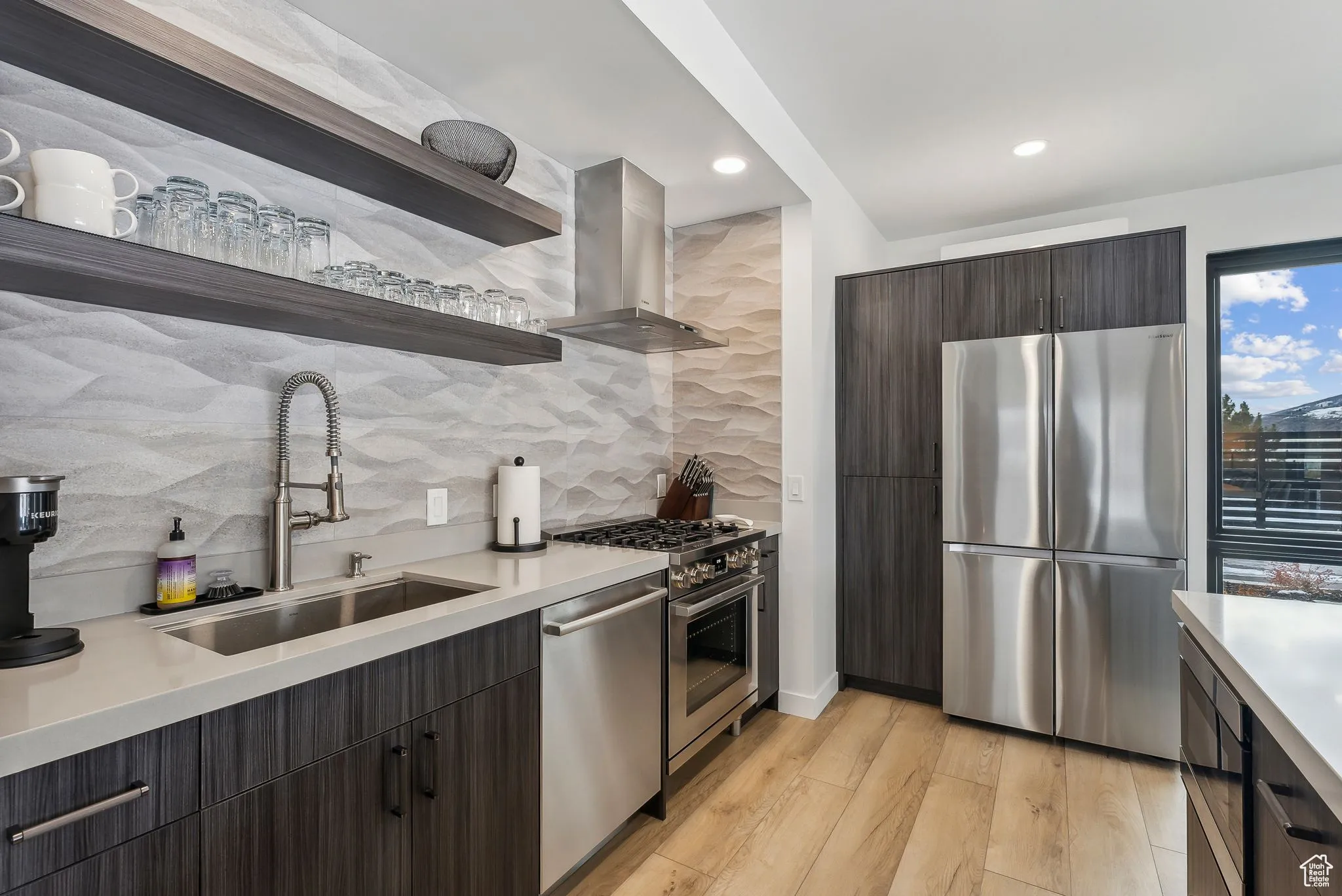 Kitchen featuring dark brown cabinetry, sink, wall chimney exhaust hood, light hardwood / wood-style flooring, and appliances with stainless steel finishes