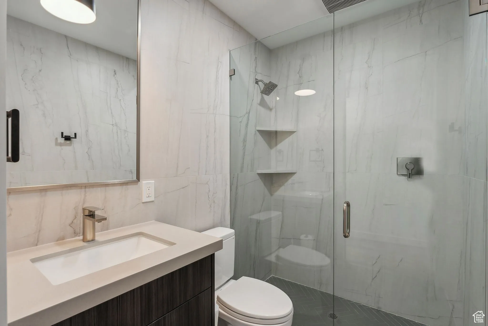 Bathroom featuring an enclosed shower, vanity, toilet, and tile walls