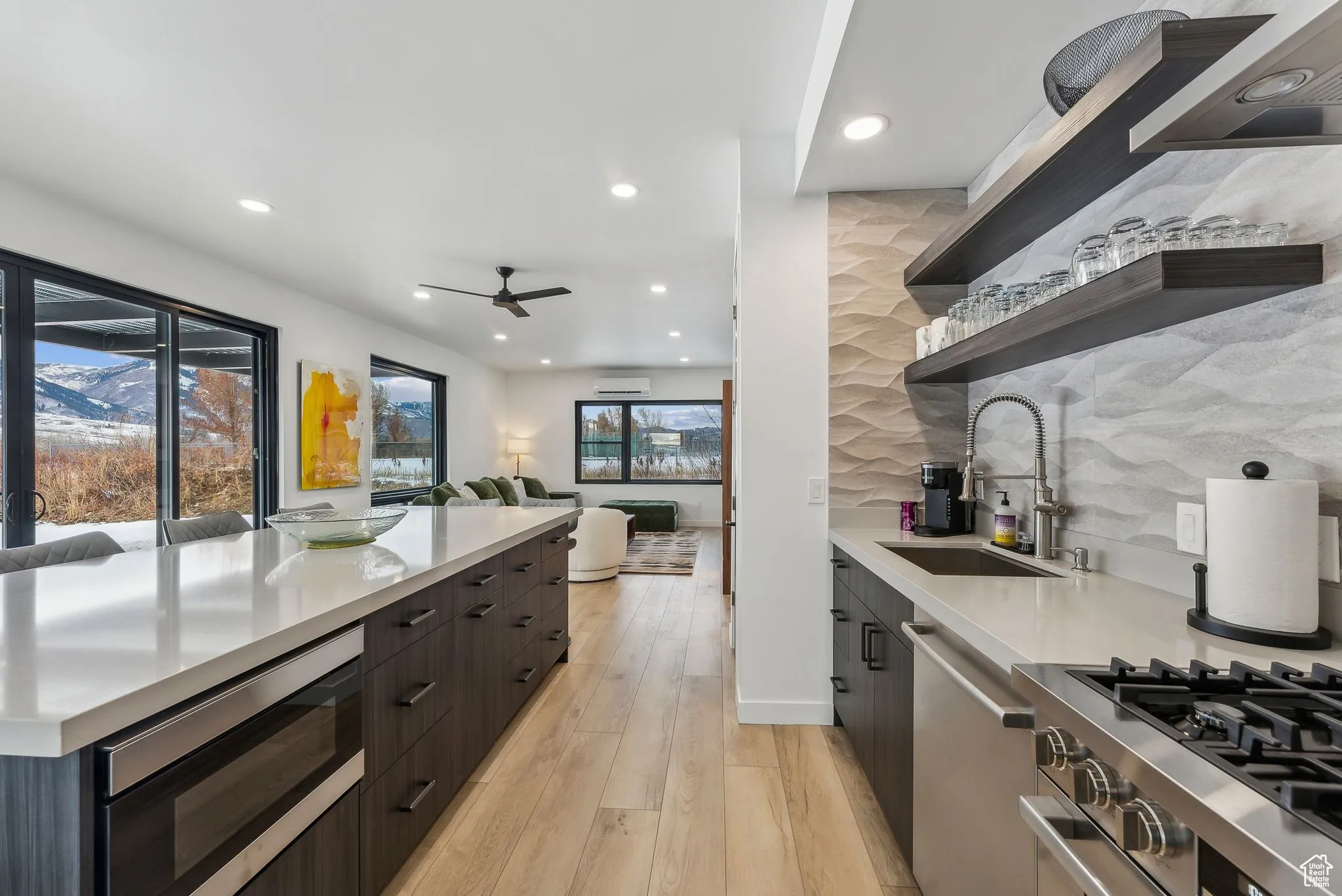 Kitchen with decorative backsplash, appliances with stainless steel finishes, light wood-type flooring, ceiling fan, and sink