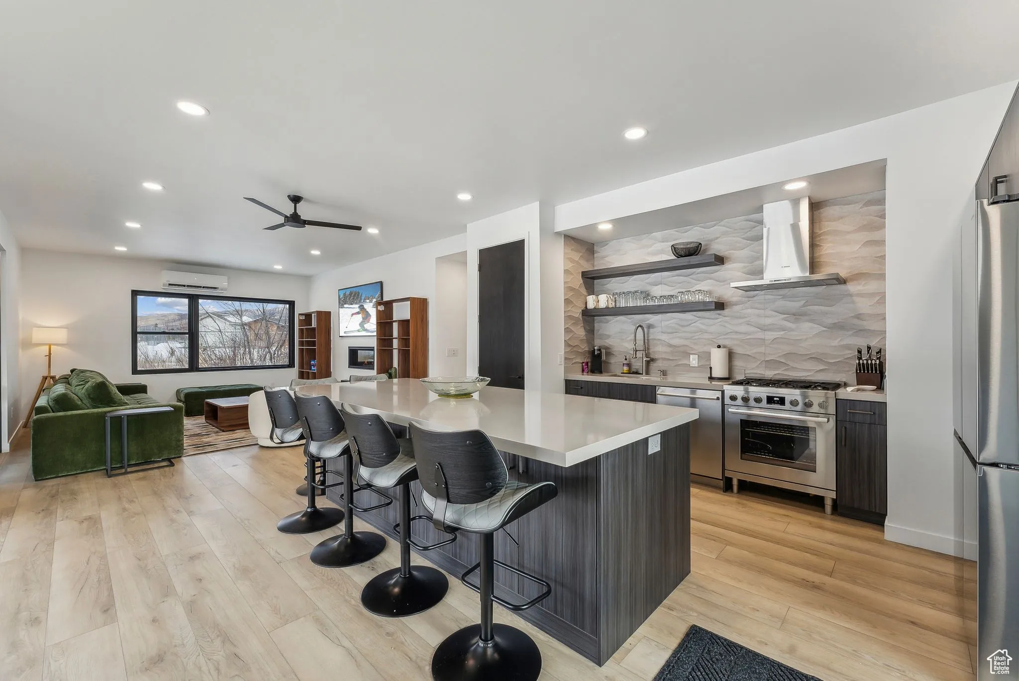 Kitchen with light wood-type flooring, stainless steel appliances, exhaust hood, an AC wall unit, and a breakfast bar area