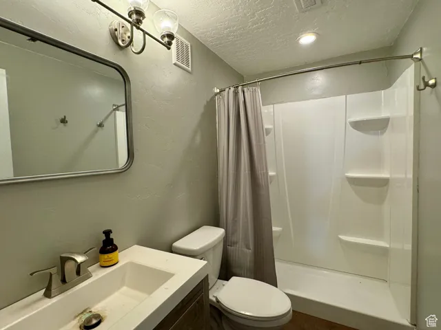 Bathroom featuring a textured ceiling, toilet, vanity, and curtained shower