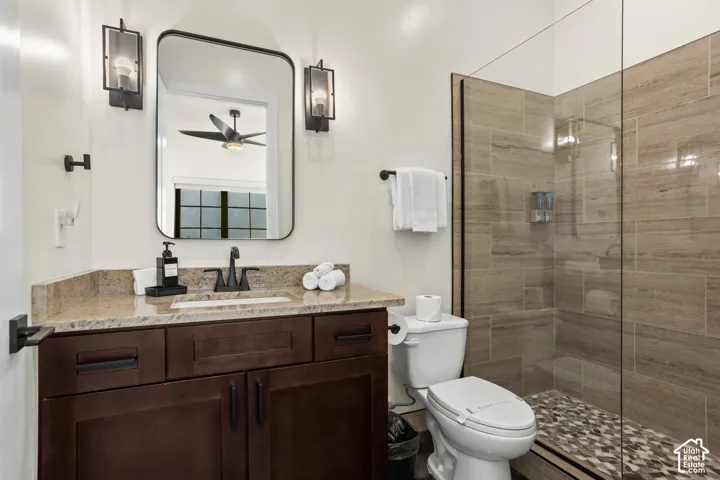One of 6 full baths, with a wood vanity and a tiled walk-in shower with a pebble floor.