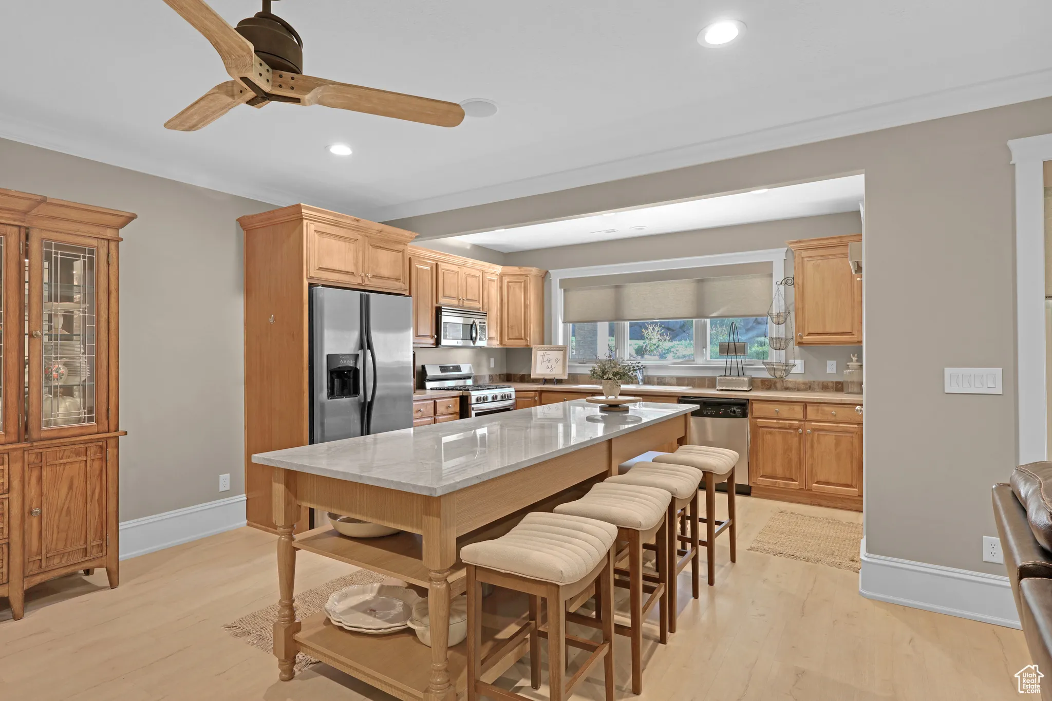 Downstairs, secondary, kitchen featuring a breakfast bar area, appliances with stainless steel finishes, light stone countertops, light brown cabinetry, and light wood-type flooring
