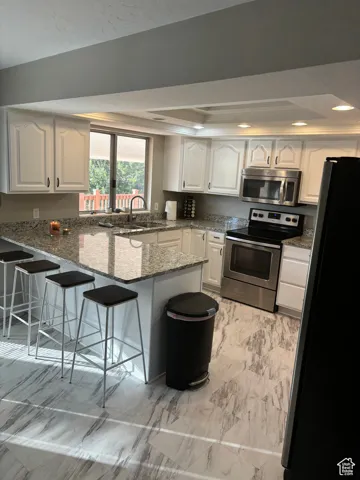 Kitchen featuring granite counters, a kitchen bar, kitchen peninsula, white cabinetry, and stainless steel appliances