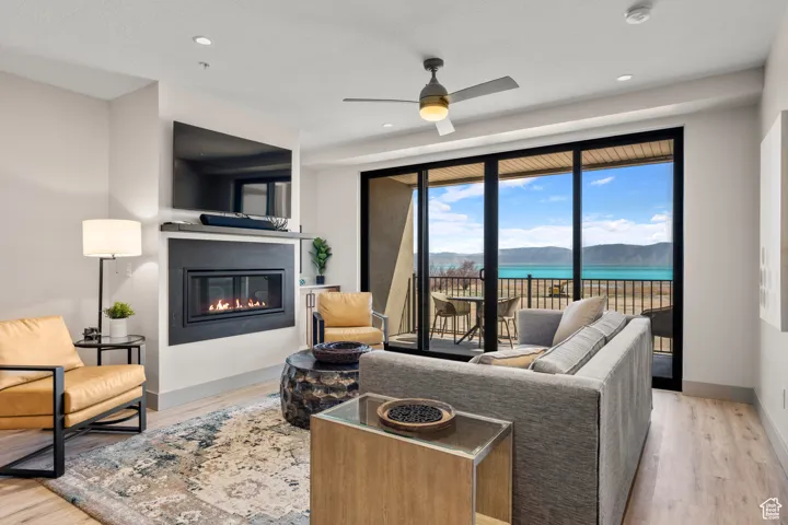 Living area featuring a glass covered fireplace, wood finished floors, ceiling fan, baseboards, and recessed lighting