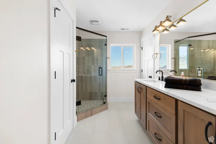 Bathroom featuring double vanity, visible vents, a sink, a shower stall, and baseboards