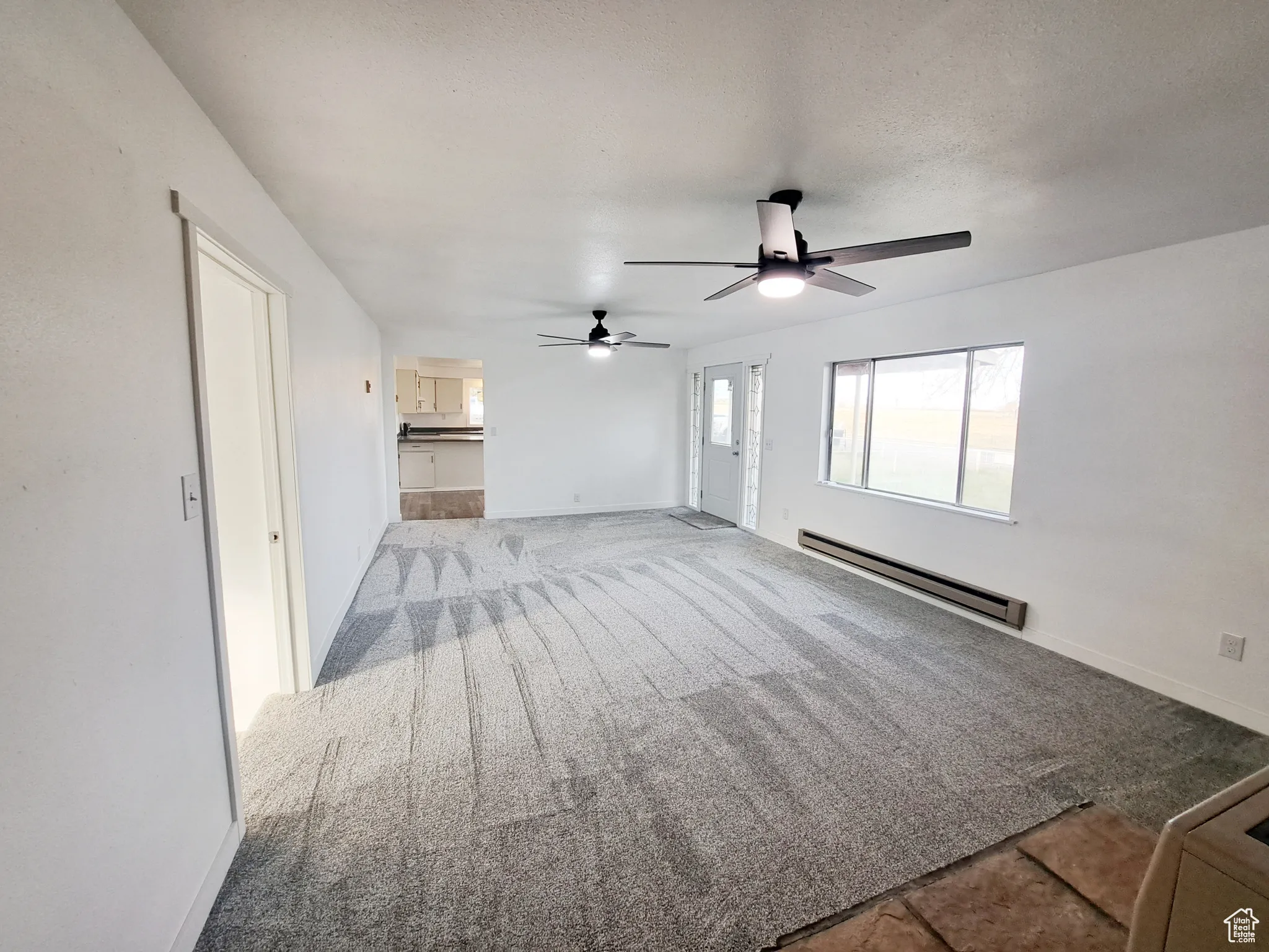 Living room featuring new light carpet, a textured ceiling,  new paint, baseboard heating, and ceiling fan