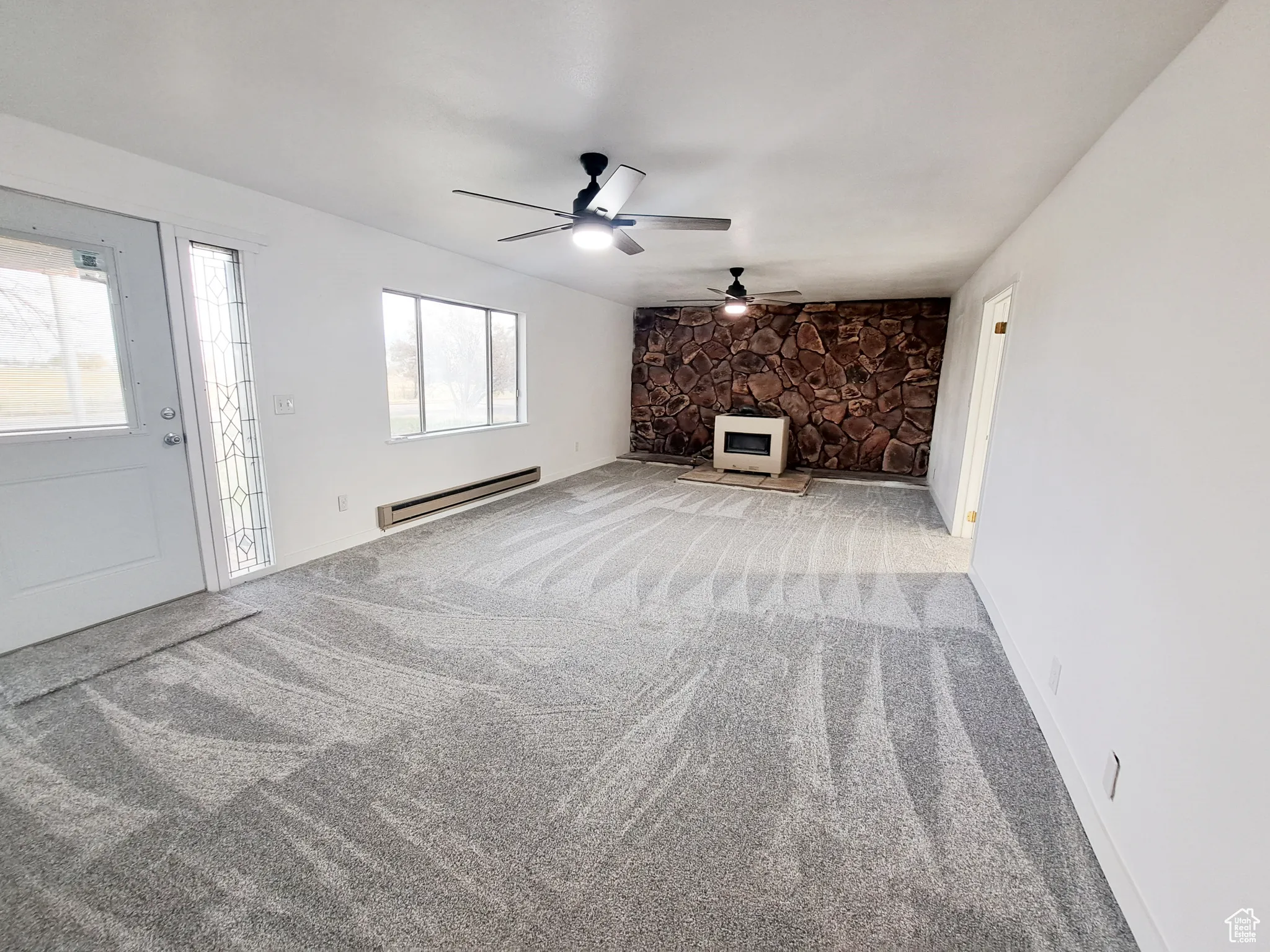 Living room featuring new carpet floors, baseboard heating, ceiling fan, new paint, and plenty of natural light