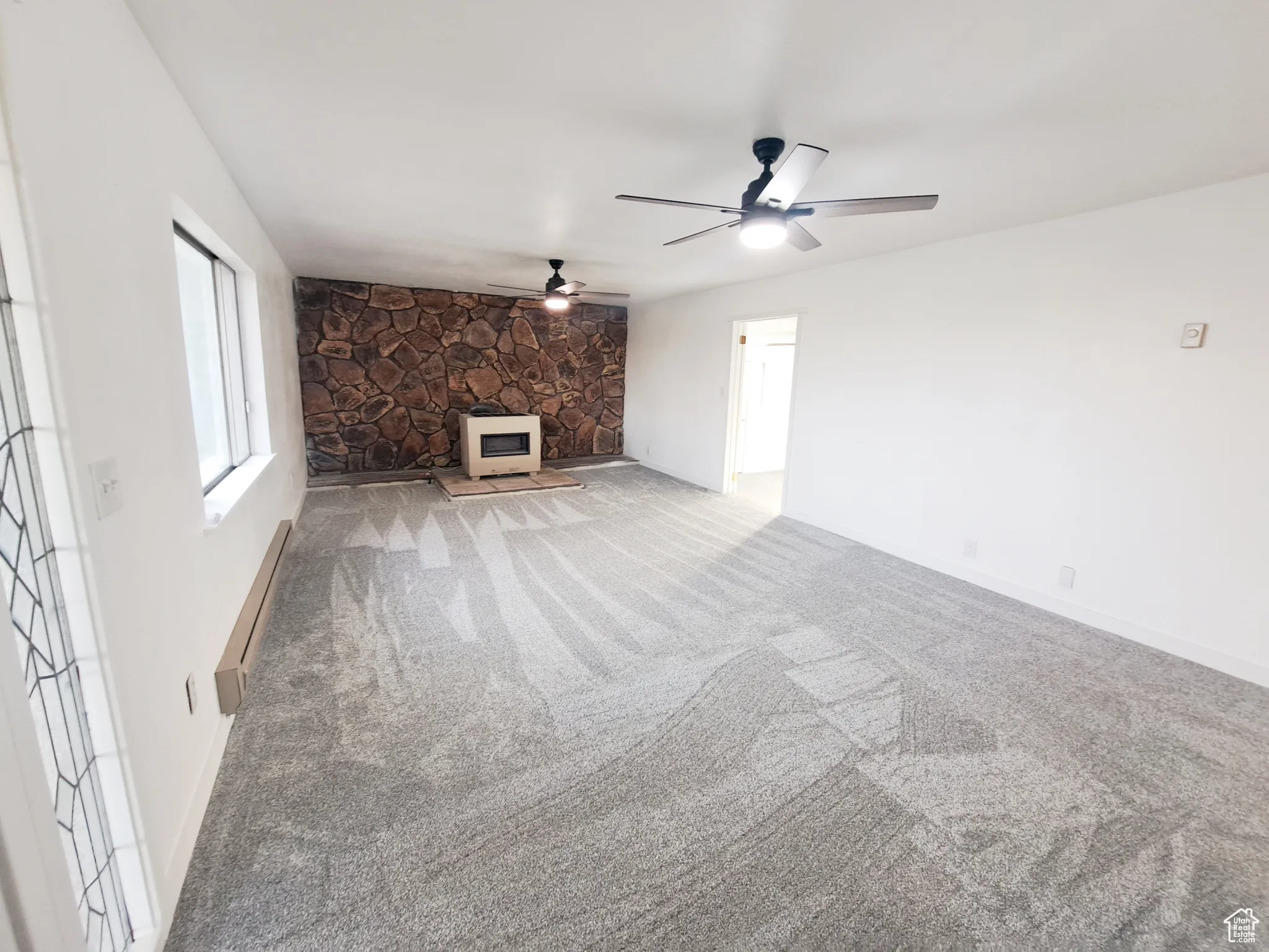 Living room featuring a heating unit, a propane fireplace, New light colored carpet, baseboard heating, ceiling fan, and new Paint.