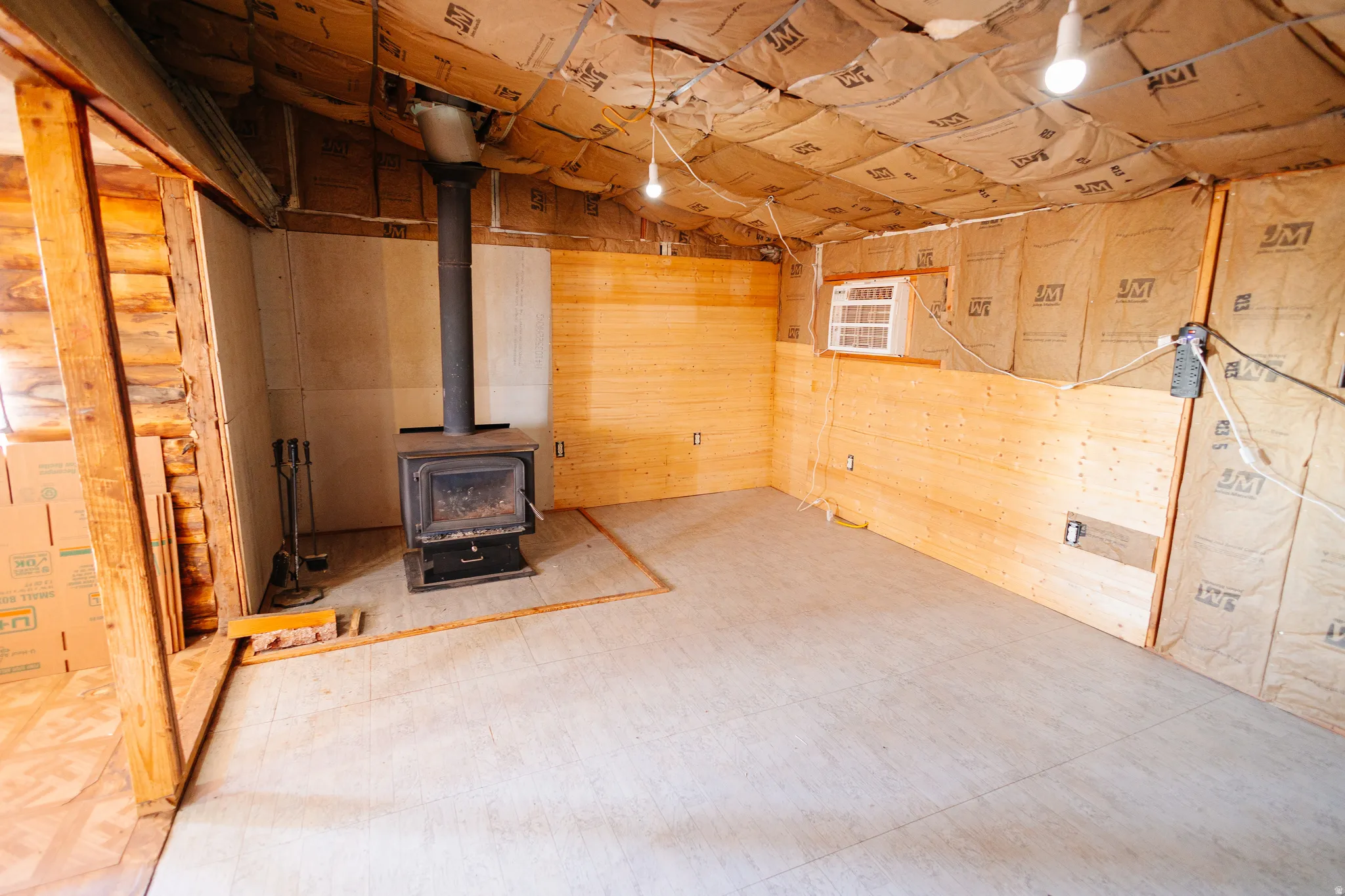 Below grade area featuring a wood stove, wooden walls, an AC wall unit, and tile patterned floors