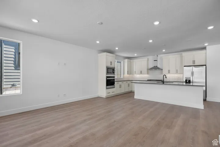 Kitchen featuring white cabinets, wall chimney exhaust hood (work in progress),, light wood-type flooring, and stainless steel appliances