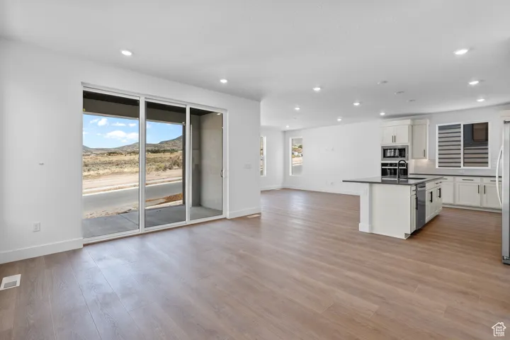 Kitchen featuring sink, stainless steel appliances, an island with sink, light hardwood / wood-style floors, and white cabinets