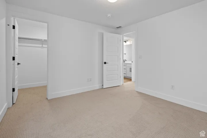 Unfurnished bedroom with a walk in closet, a closet, light colored carpet, and a textured ceiling