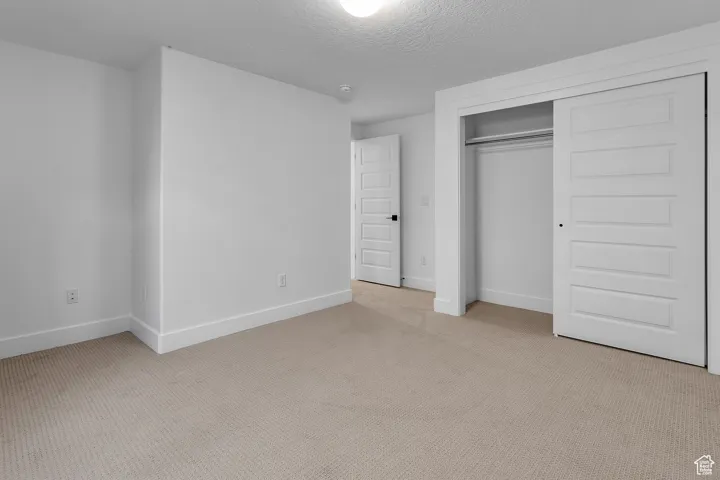 Unfurnished bedroom with light colored carpet, a textured ceiling, and a closet