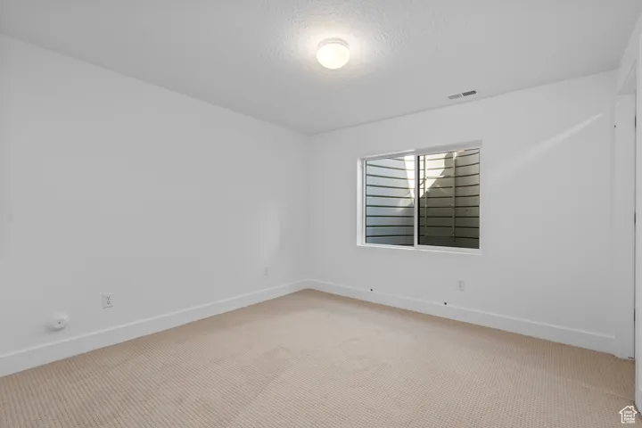 Empty room with light carpet and a textured ceiling