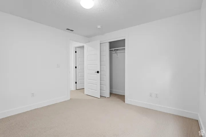 Unfurnished bedroom featuring light carpet, a textured ceiling, and a closet