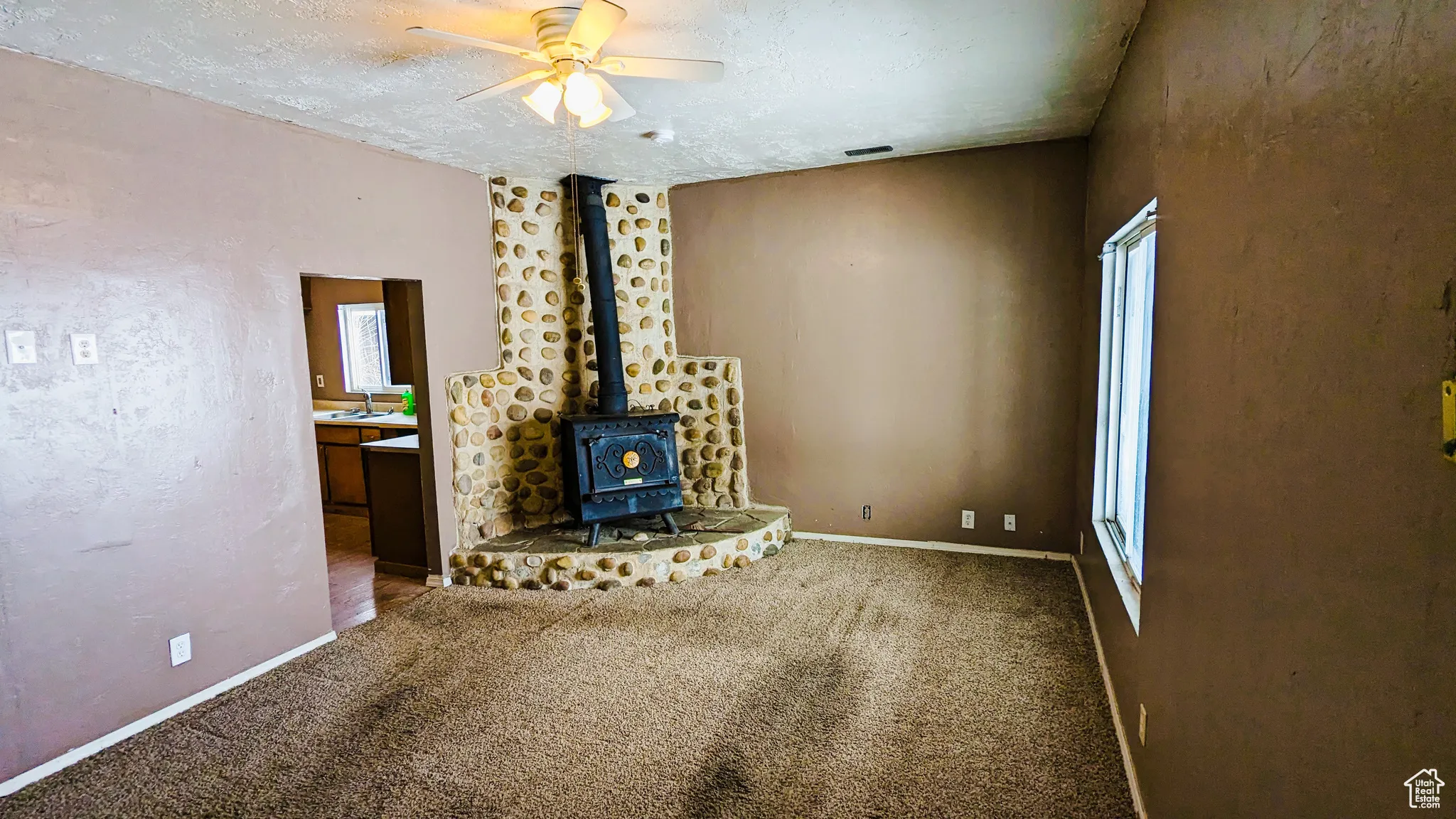 Unfurnished living room with carpet, a wood stove, sink, ceiling fan, and a textured ceiling