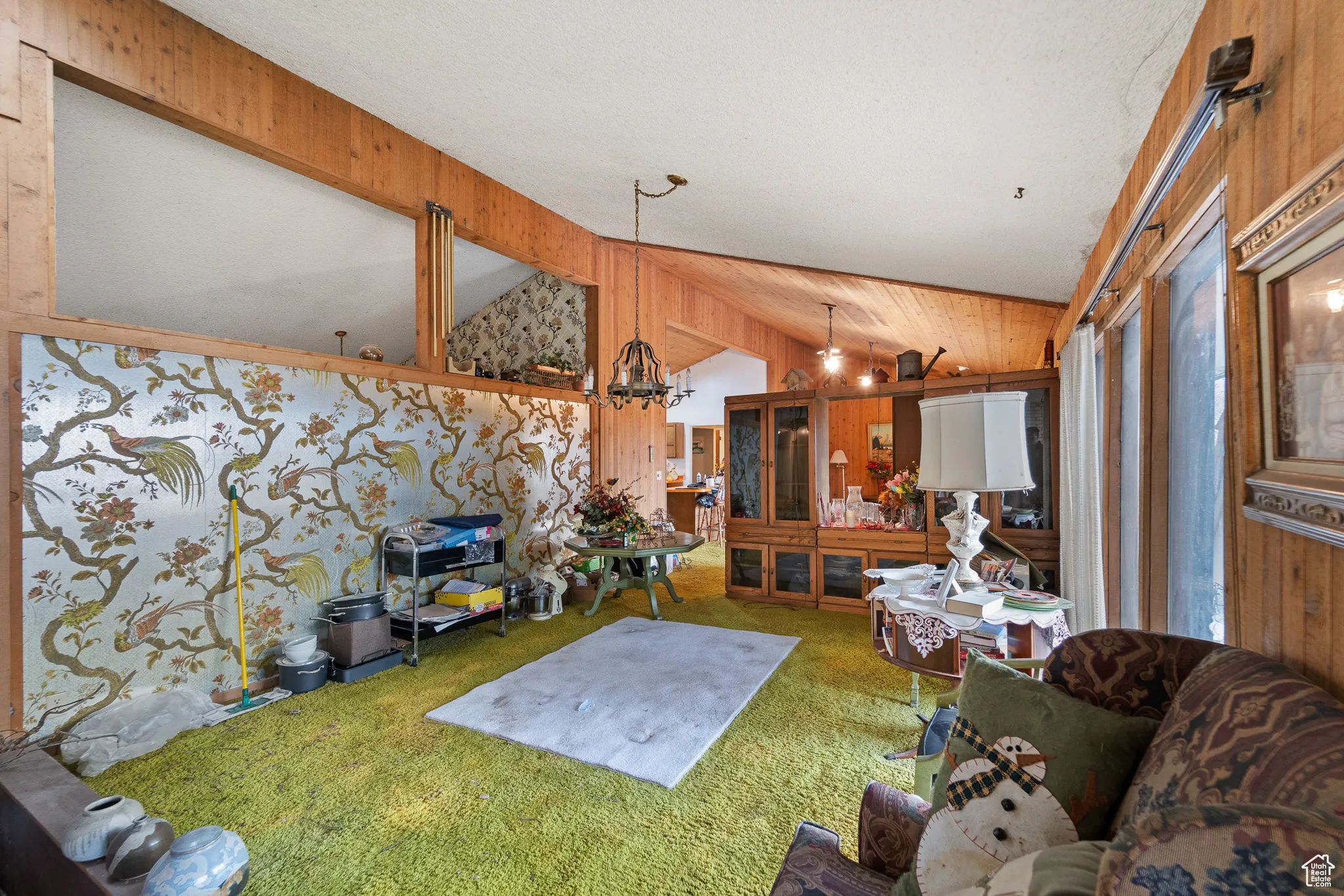Carpeted living room featuring wood walls, vaulted ceiling, and a notable chandelier