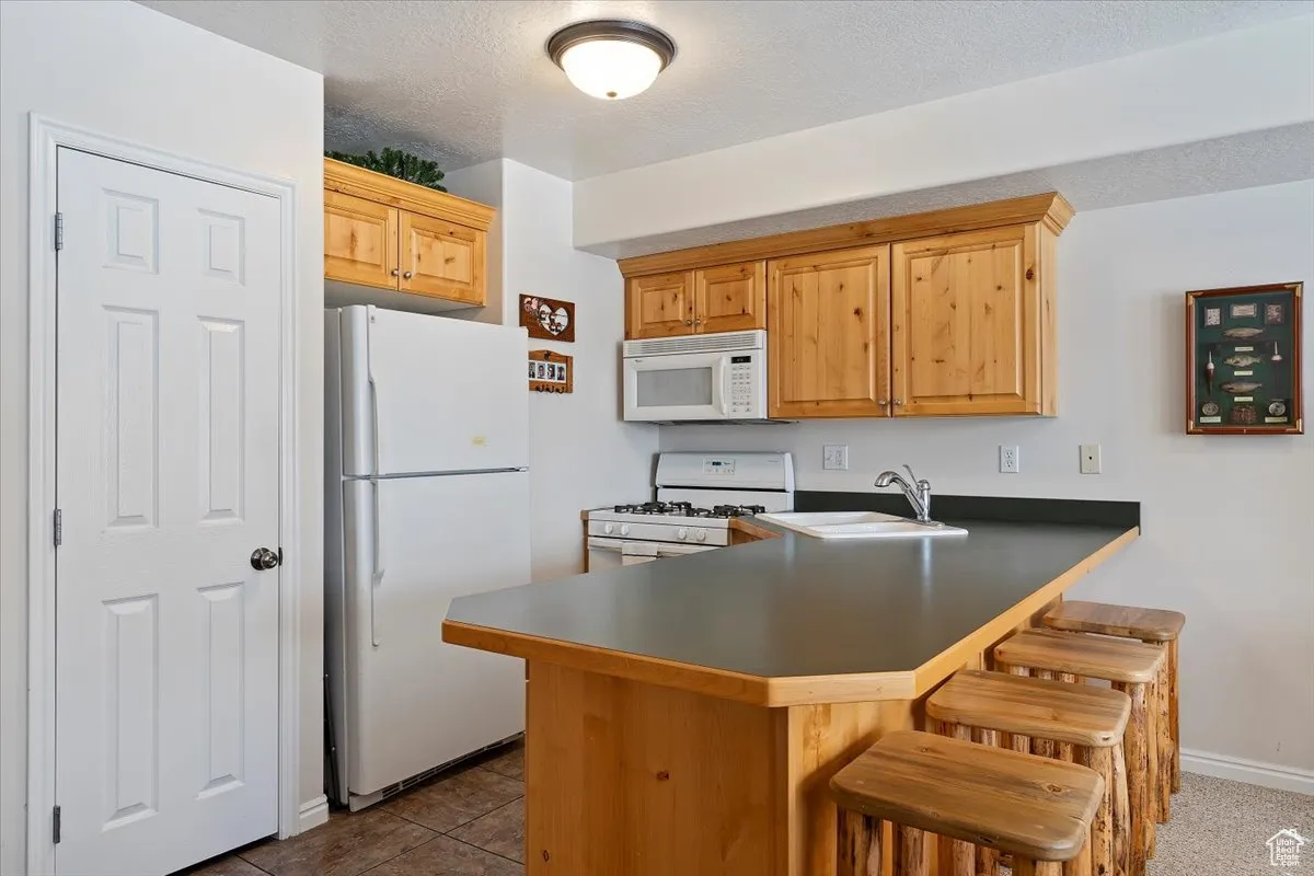 Kitchen featuring sink, a kitchen breakfast bar, kitchen peninsula, a textured ceiling, and white appliances