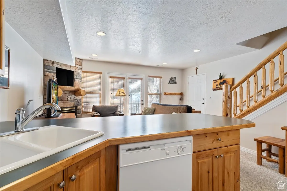 Kitchen featuring sink, white dishwasher, a textured ceiling, light carpet, and a fireplace