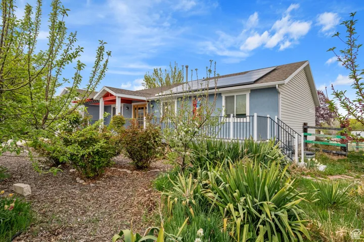 View of front of house featuring a wooden deck, solar panels, and roof with shingles