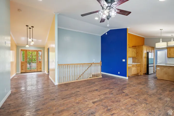 Unfurnished living room with lofted ceiling, crown molding, baseboards, dark wood-type flooring, and a ceiling fan