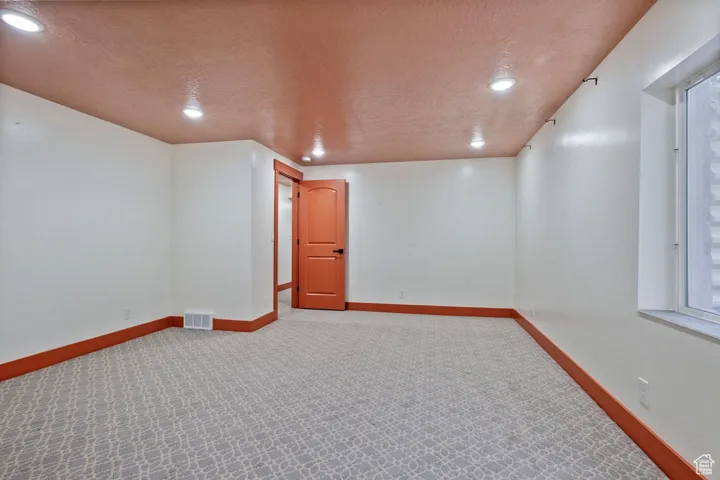 Empty room with a textured ceiling, visible vents, baseboards, recessed lighting, and carpet