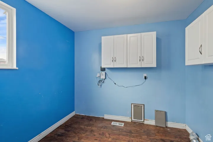 Clothes washing area with dark wood-style floors, baseboards, and visible vents