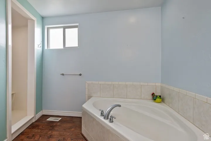 Full bathroom with wood finished floors, a garden tub, visible vents, and baseboards