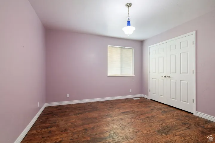 Unfurnished bedroom featuring dark wood-style flooring, a closet, and baseboards