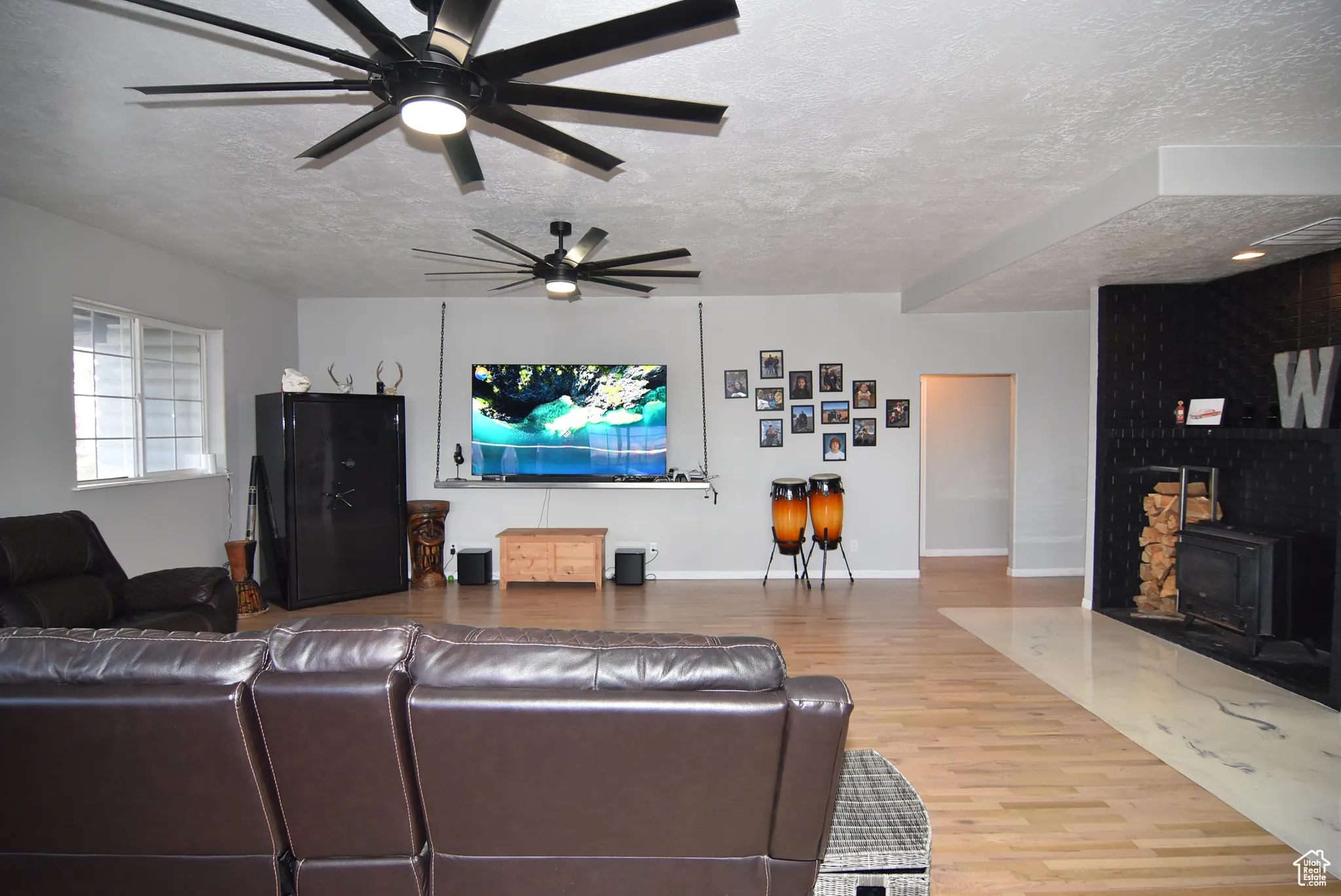 Living room with a textured ceiling, hardwood / wood-style flooring, a wood stove, and ceiling fan