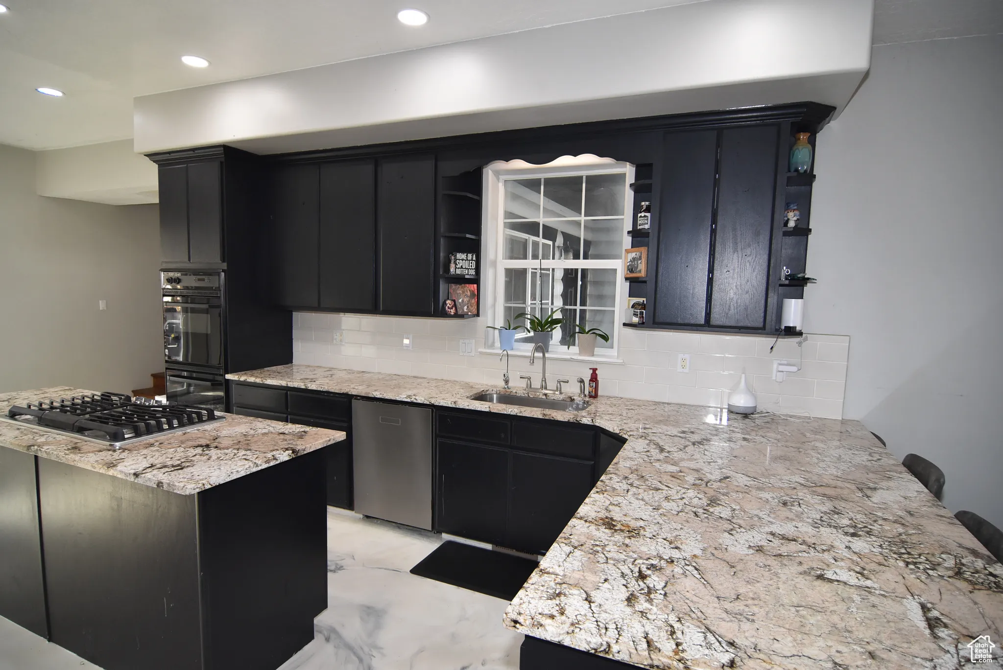 Kitchen featuring sink, decorative backsplash, light stone countertops, kitchen peninsula, and stainless steel appliances