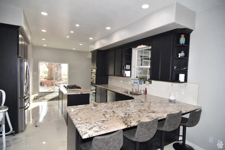 Kitchen with light stone counters, kitchen peninsula, sink, and tasteful backsplash