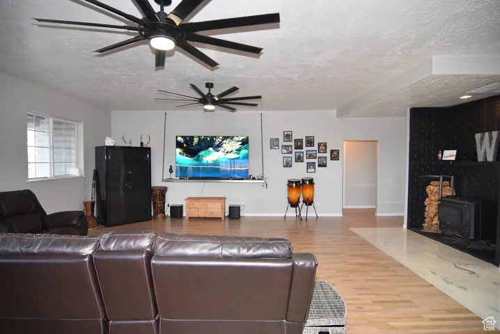 Living room with hardwood / wood-style flooring, ceiling fan, a wood stove, and a textured ceiling