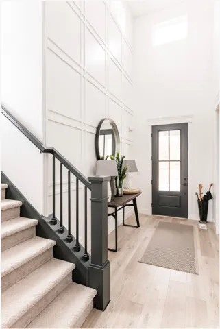 Two-story entryway featuring a custom accent wall with applied molding, light wood-finish flooring, and a staircase with a dark wood newel post and balusters