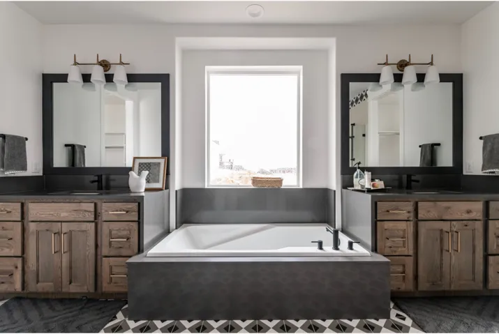 Bathroom featuring a built-in soaking tub beneath a window, flanked by two wood-finish vanities with dark countertops and integrated sinks